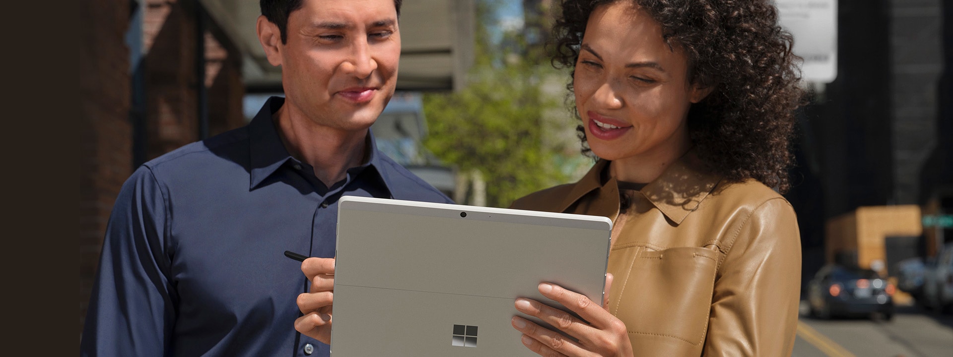 Dos personas afuera, en la acera de una ciudad metropolitana, miran a la pantalla de su Surface Pro X en modo tableta