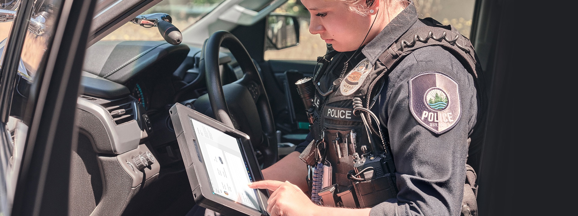 A policewoman is seen sitting in the passenger seat of her patrol car while using a Surface Pro device