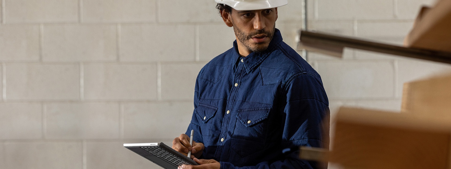 Um colaborador com um capacete num cenário industrial a segurar num Surface Go 2 em modo de tablet