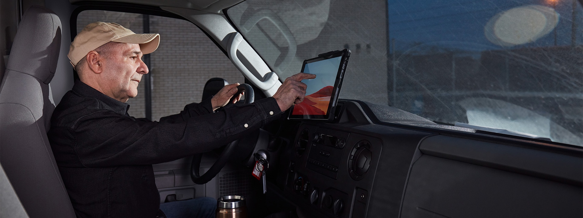 Een vrachtwagenchauffeur zit in de cabine van zijn truck en gebruikt het aanraakscherm van een Surface Pro 7+