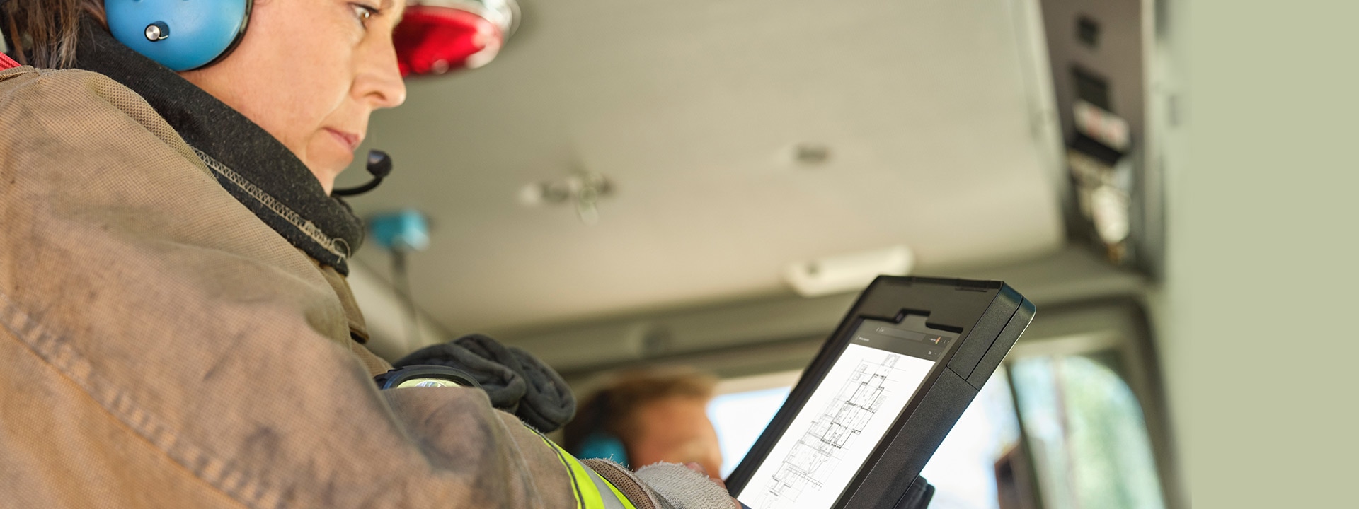A woman dressed in bunker gear is observed looking at the screen of her Surface device while seated in a fire truck