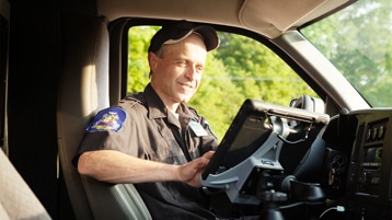 Un agente de seguridad pública trabajando en una tablet en su vehículo.