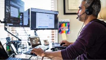 Osoba s náhlavní soupravou pracující na dvou monitorech stolního počítače. 