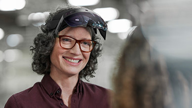 Henkilö hymyilee ja käyttää otsalleen tuettua HoloLens 2:ta.