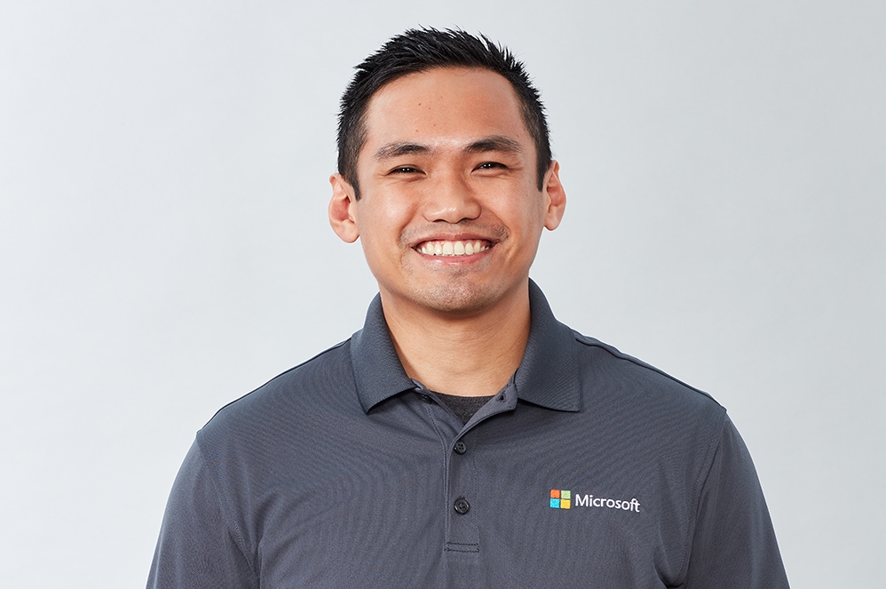 Ryan, a Microsoft business product expert, smiles while wearing a shirt with a Microsoft logo.