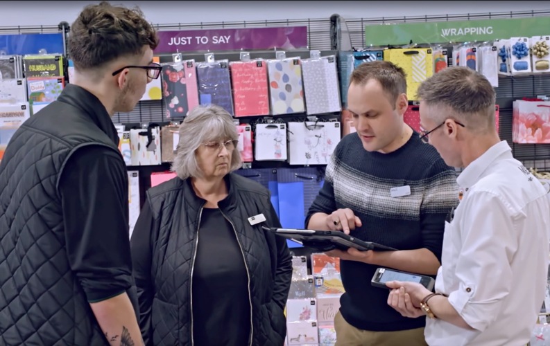 Four employees having a meeting in the gift wrap aisle of a store.