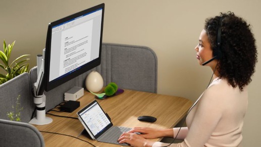 Una persona con auriculares escribiendo en un teclado conectado a una tableta y un monitor de escritorio.