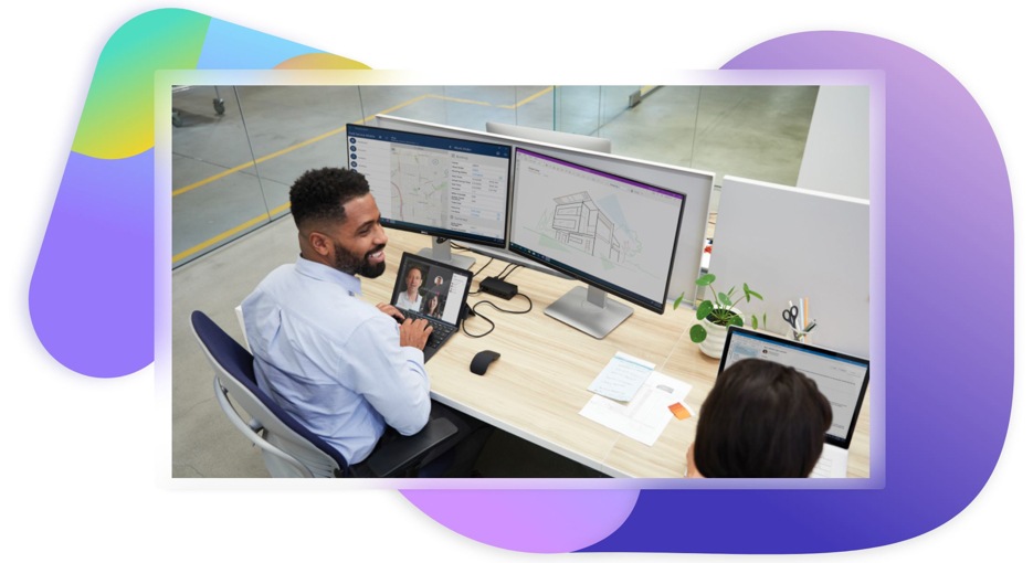 Two people at a desk while one is on a Teams video call and looking at architectural designs and maps across two monitors.