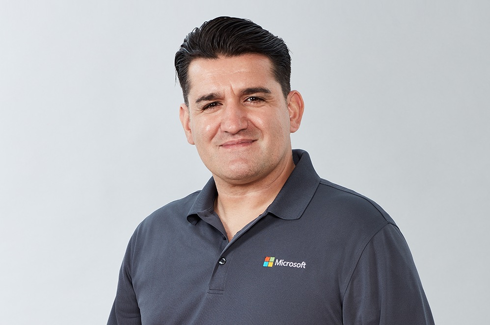 Erol, a Microsoft business product expert, smiles while wearing a shirt with a Microsoft logo.