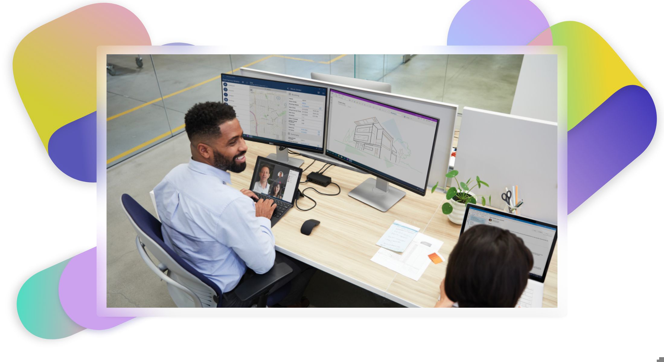 Two people at a desk while one is on a Teams video call and looking at architectural designs and maps across two monitors.