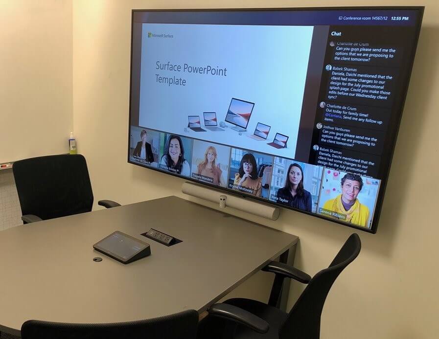 An empty focus room with a wall-mounted computer screen showing a user joined to a meeting with a PowerPoint deck on display.
