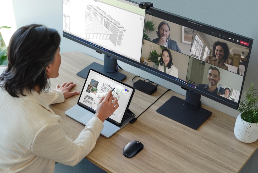 Eine Dame sitzt an ihrem Schreibtisch und arbeitet mit ihrem Surface Laptop Studio. Ein Monitor zeigt, dass sie gerade an einem Teams Meeting teilnimmt.