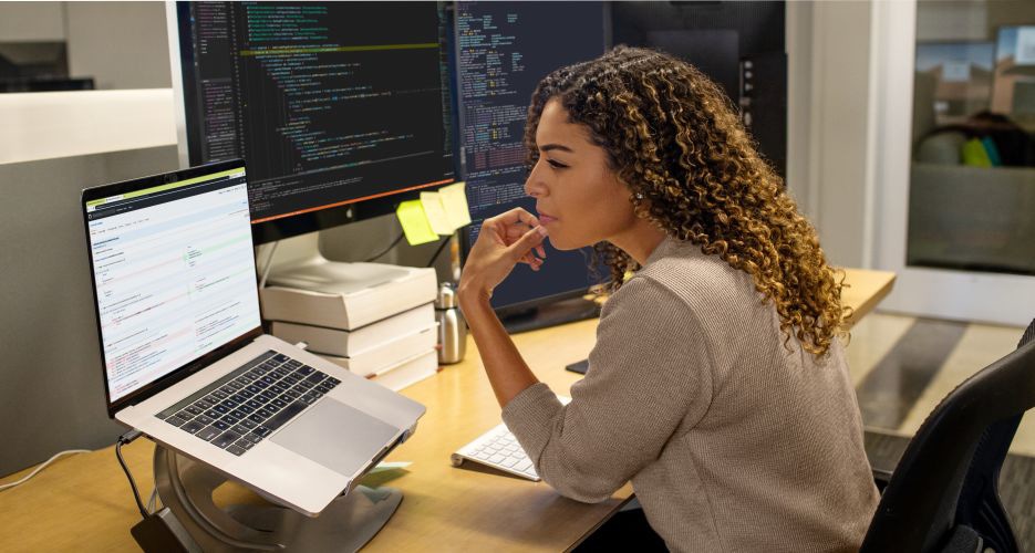 Una persona lavora a una scrivania con due monitor collegati a un portatile.