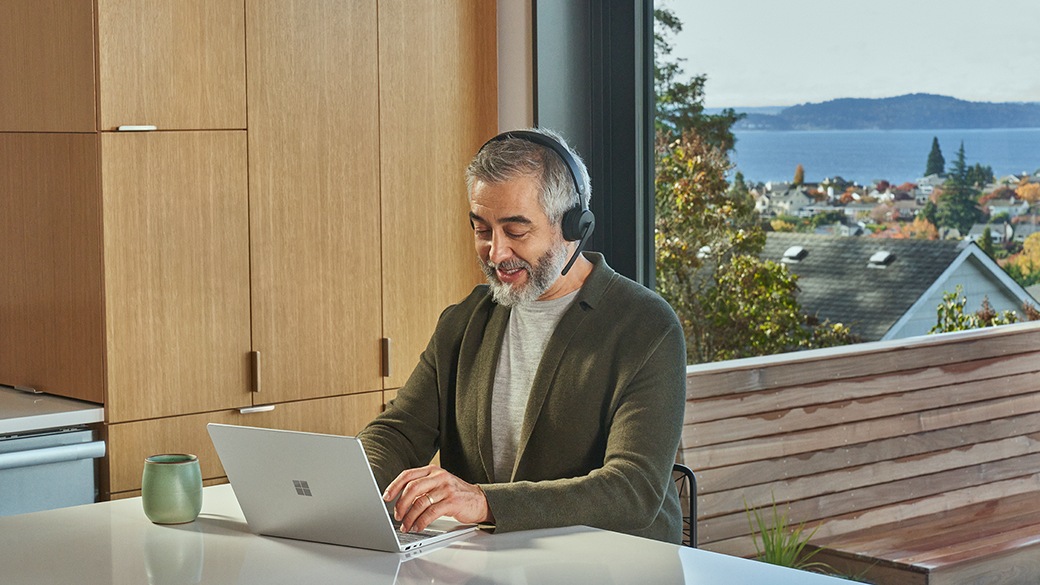 A person on a video call uses Surface Laptop Go 2 for Business and a Microsoft Modern Wireless Headset for Business.