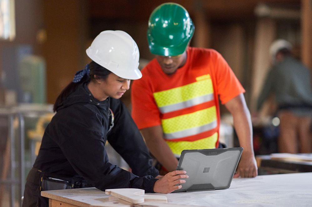 People wearing safety helmets use Surface Laptop Go 2 for Business from a construction worksite.