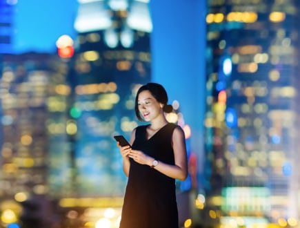 A person smiling at their phone with a city skyline in the background.