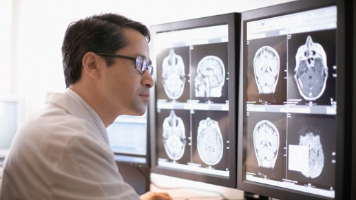 Una persona analizando escáneres cerebrales mostrados en dos monitores