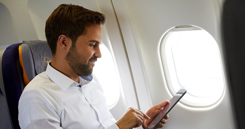 Ein Mann in Hemd blickt im Flugzeug auf ein Tablet.
