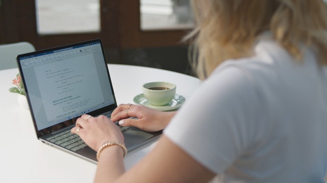 En kvinne arbeider med et skuespill og bruker tastaturet i full størrelse på Surface Laptop Go 2.