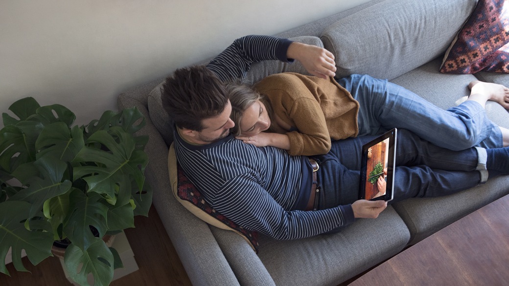 Man and girl laying together on a sofa watching a video on their Surface Pro