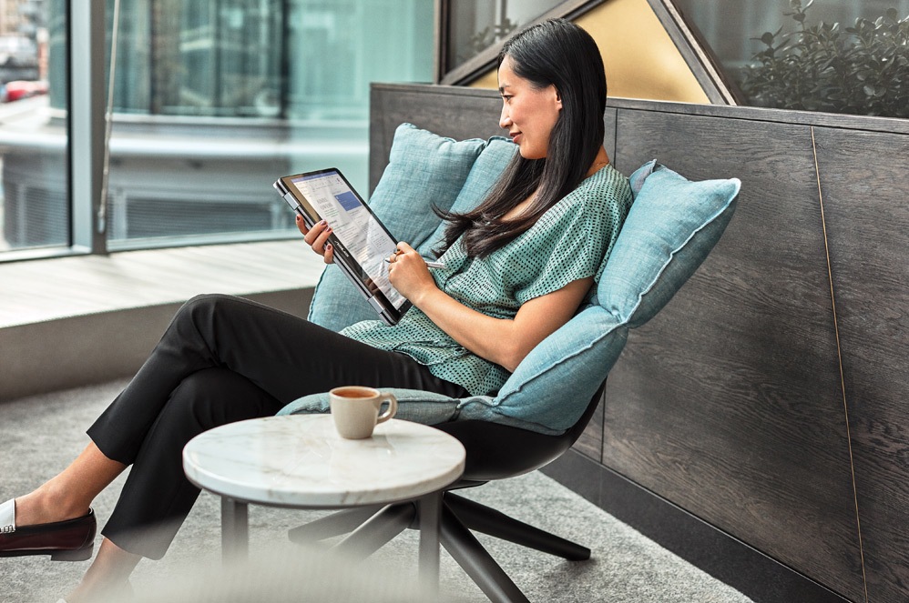 A Surface Pro X sits open on a chair outside atop an apartment patio with a pen in front of it and OneDrive on the screen