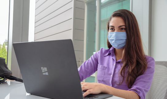 A person wearing a mask using a laptop.
